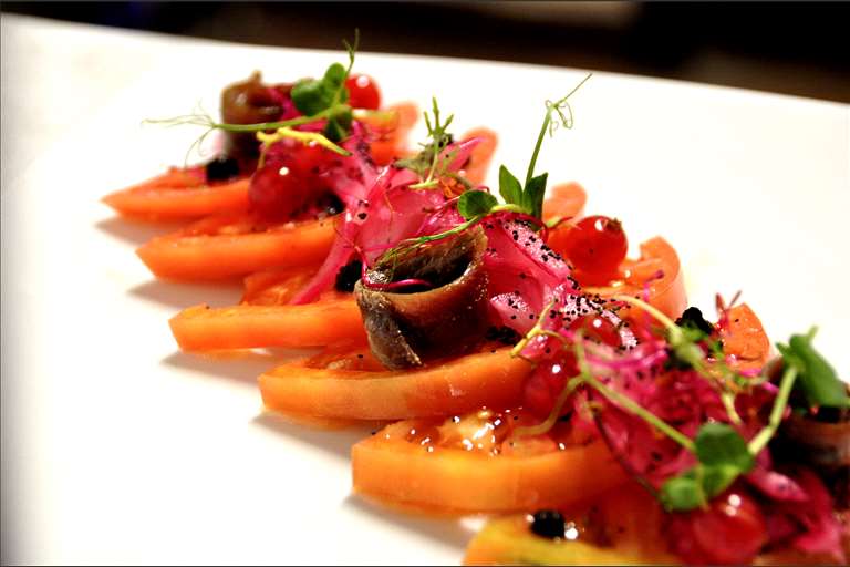Ensalada de Tomate Rosa de Barbastro, anchoas y olivas negras, coronada de cebolla roja encurtida.